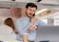 Empleado revisando su horario laboral mientras trabaja en oficina y habla por teléfono.