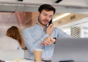 Empleado revisando su horario laboral mientras trabaja en oficina y habla por teléfono.