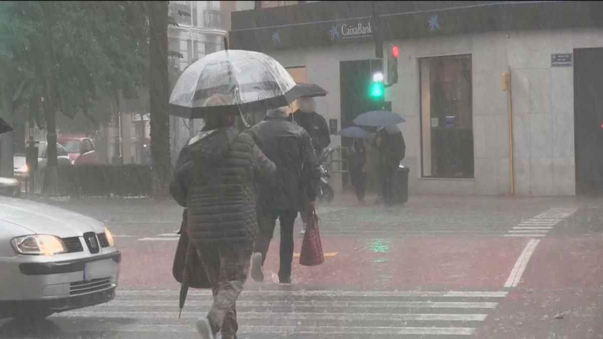 Personas caminando bajo una intensa lluvia en una calle de Madrid con paraguas.