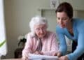 Mujer ayudando a una persona mayor con documentos sobre la deducción por convivir con mayores de 65 años.