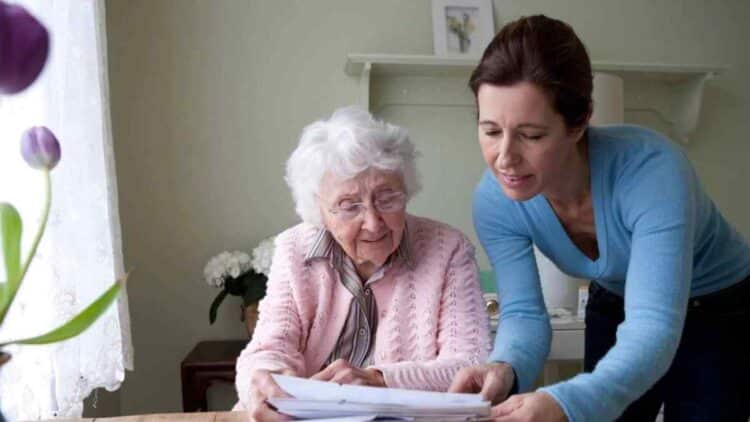 Mujer ayudando a una persona mayor con documentos sobre la deducción por convivir con mayores de 65 años.
