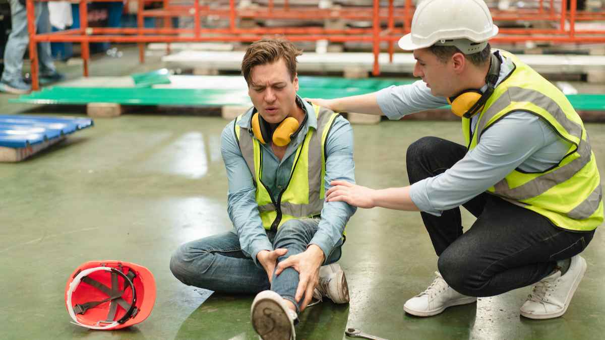 Trabajador herido en accidente laboral siendo atendido por un compañero en una fábrica.