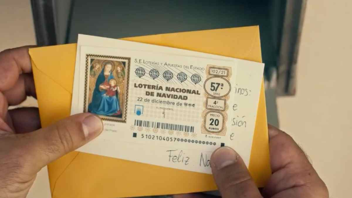 Manos sosteniendo un décimo de la Lotería de Navidad con una frase escrita en la parte trasera.