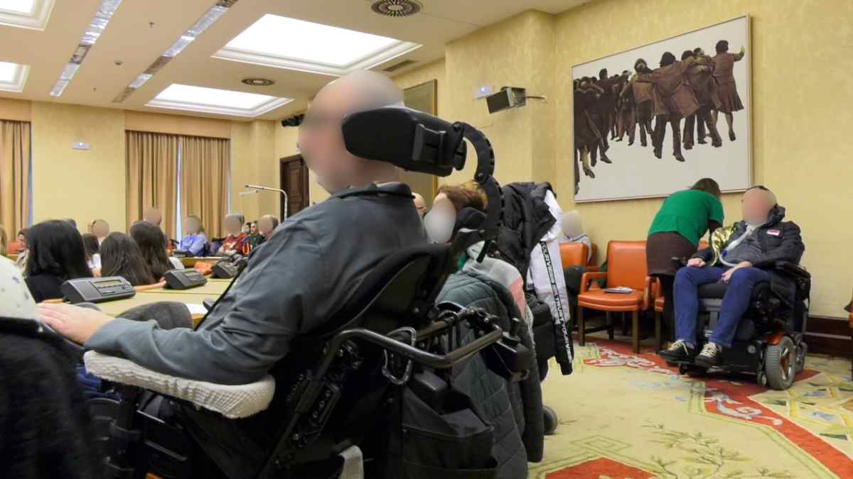 Personas con ELA y movilidad reducida en una sala institucional durante una reunión sobre dependencia extrema.