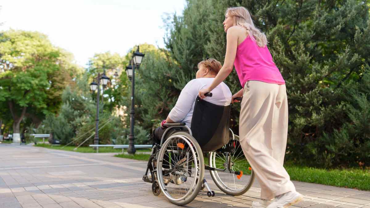 Cuidadora empujando silla de ruedas en un parque al aire libre.