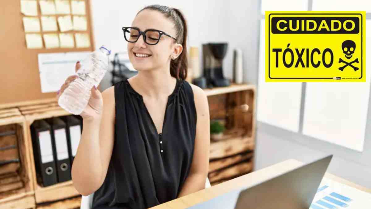 Mujer sosteniendo una botella de agua junto a un cartel de advertencia por sustancia tóxica.