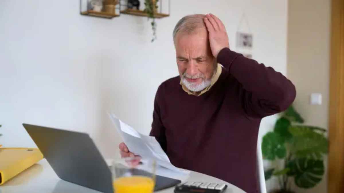 Hombre mayor preocupado revisando una carta frente al ordenador.