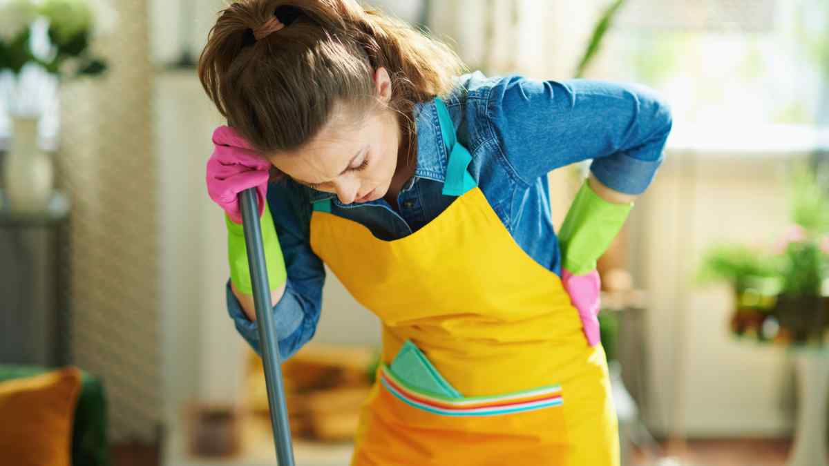 Empleada del hogar con dolor lumbar mientras realiza tareas de limpieza.
