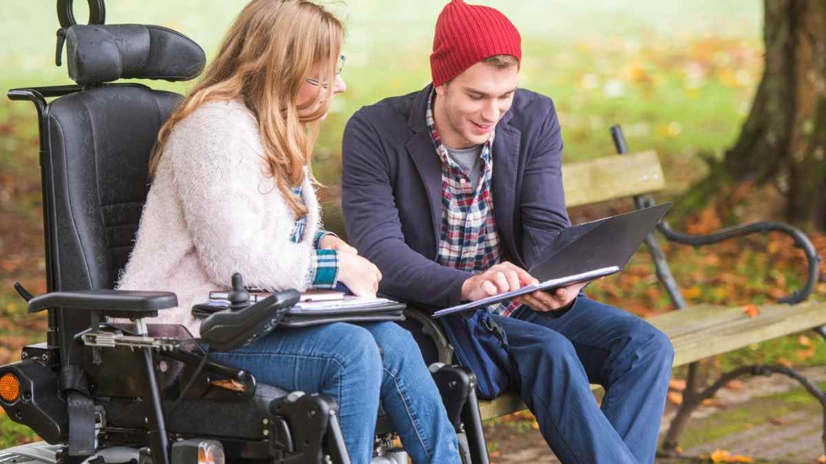 asistente personal apoyando a una persona en silla de ruedas mientras revisan documentos en un parque.