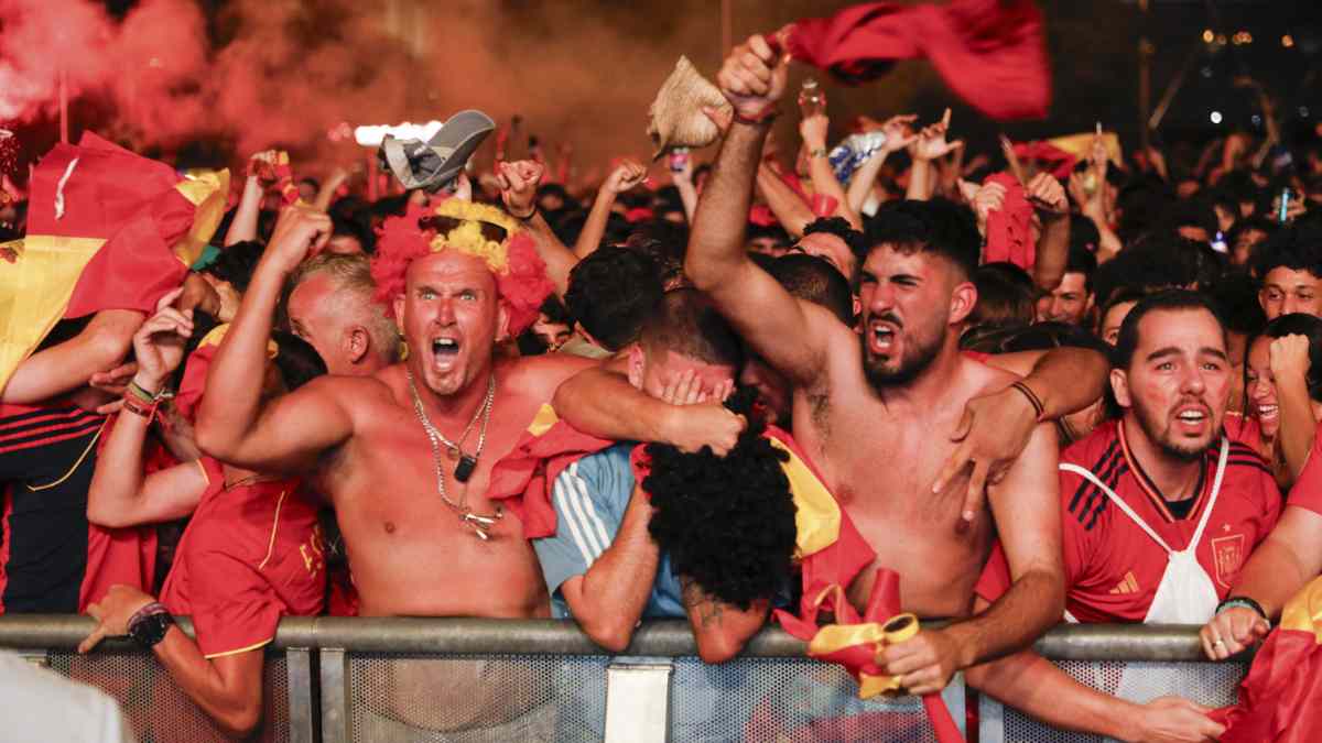 Aficionados celebrando con euforia la final de la Eurocopa entre una multitud con banderas de España.