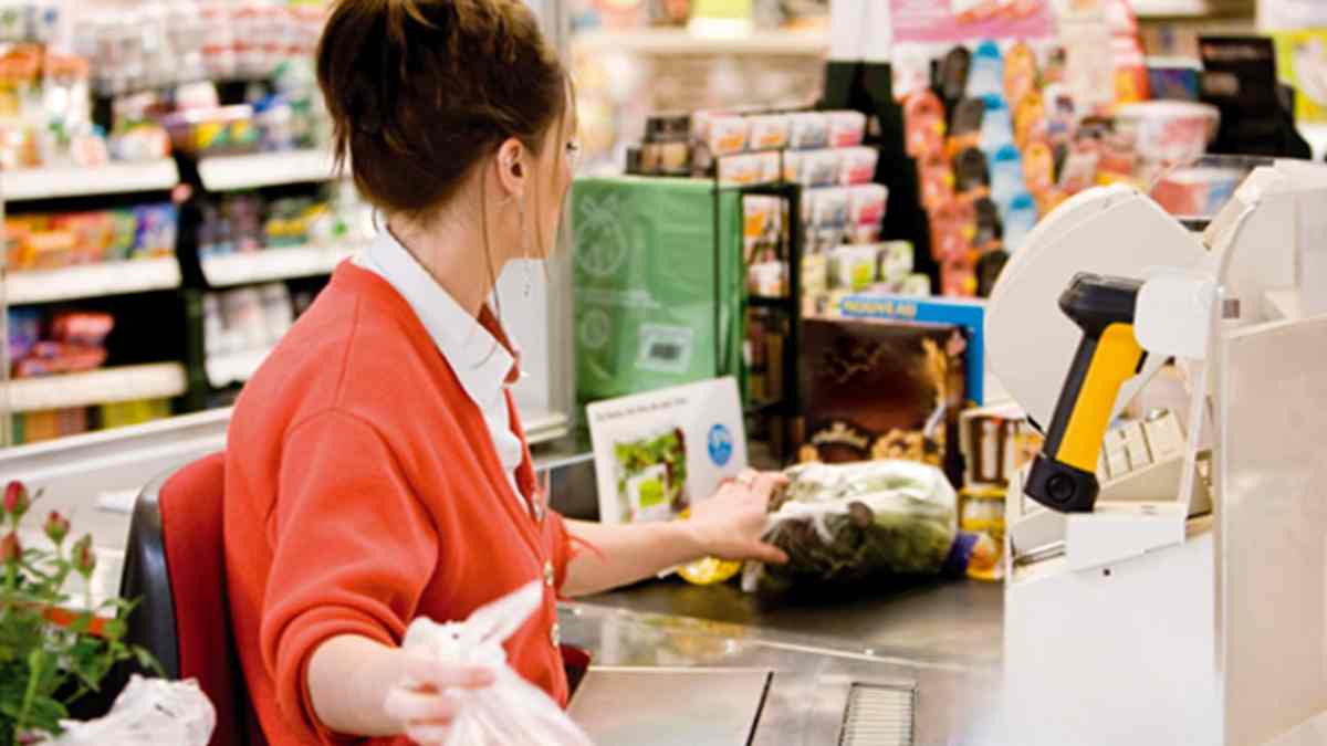 Cajera de supermercado atendiendo en la línea de caja durante su jornada laboral.
