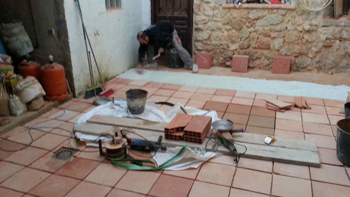 Obrero realizando reformas en un patio interior con nuevos azulejos y materiales de obra.