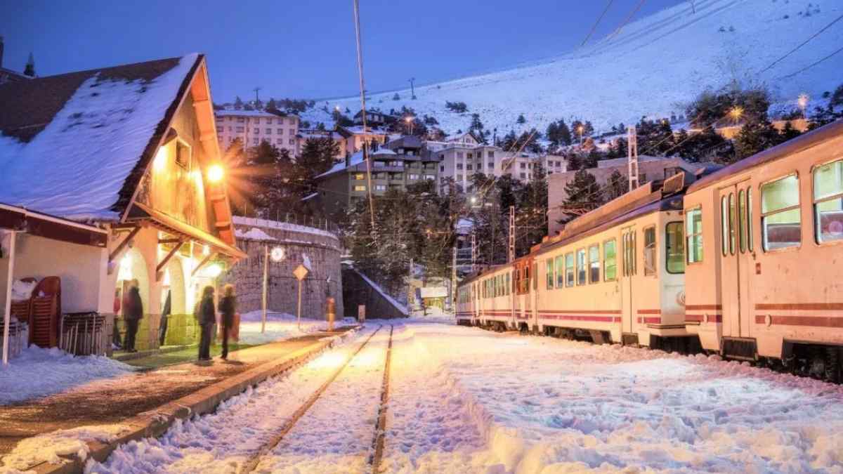 Estación de tren nevada en Navacerrada con un tren iluminado al atardecer durante la temporada de Navidad.