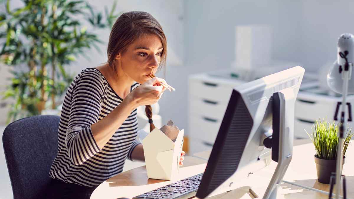 Trabajadora comiendo frente al ordenador durante la pausa de la comida en la oficina.