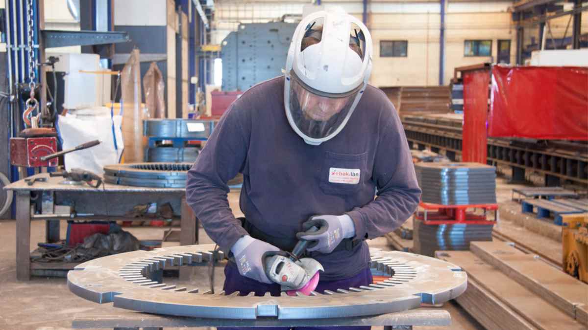 Trabajador metalúrgico rebabando una pieza en una fábrica industrial