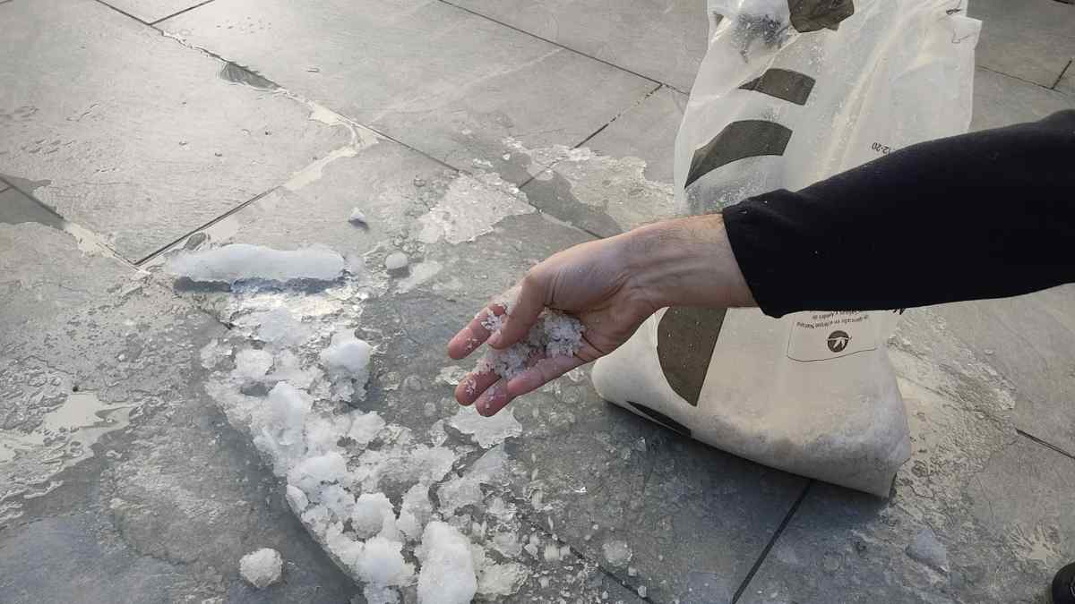 Vecino esparciendo sal en una acera helada ante la previsión de nieve y heladas