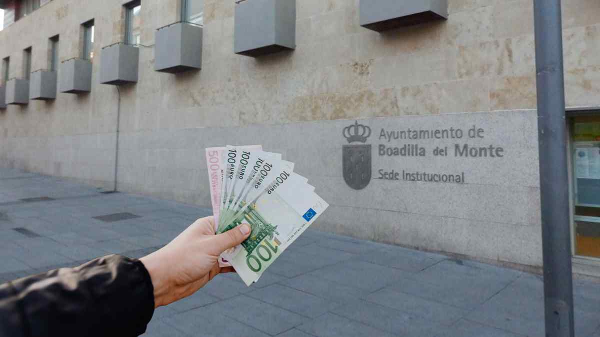 Persona mostrando billetes de euros frente al Ayuntamiento de Boadilla del Monte por ayudas de emergencia de hasta 2.000 euros
