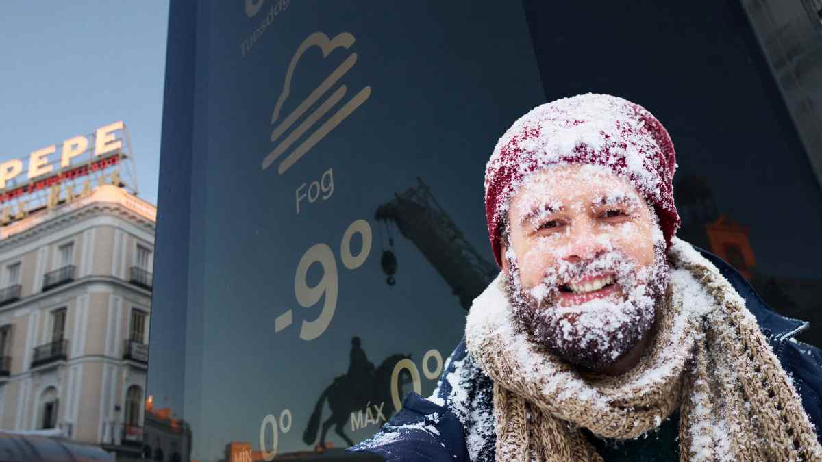 Hombre abrigado con nieve en el rostro frente a un panel meteorológico durante un episodio de frío invernal en Madrid