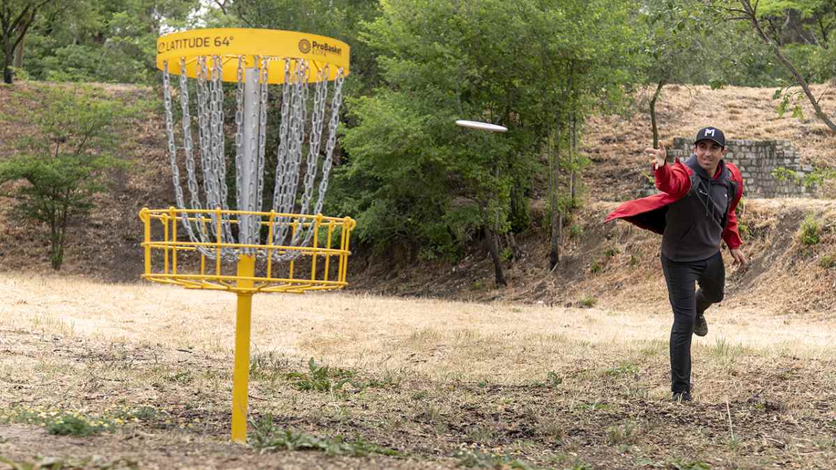 Jugador lanzando un disco hacia una canasta de disc golf en un campo al aire libre de Madrid