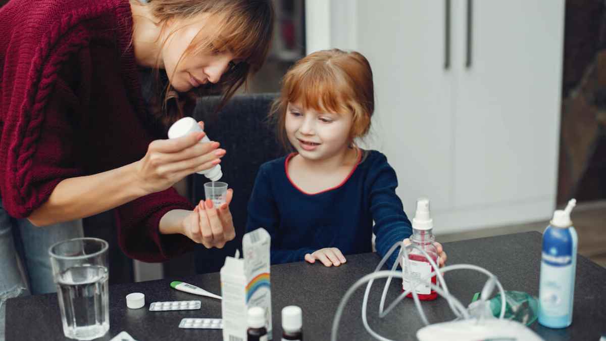 Madre administrando medicación a su hija enferma en casa durante reducción de jornada por cuidado de menor