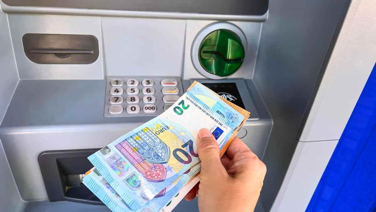 Retirada de dinero en cajero automático con billetes de euro en la mano