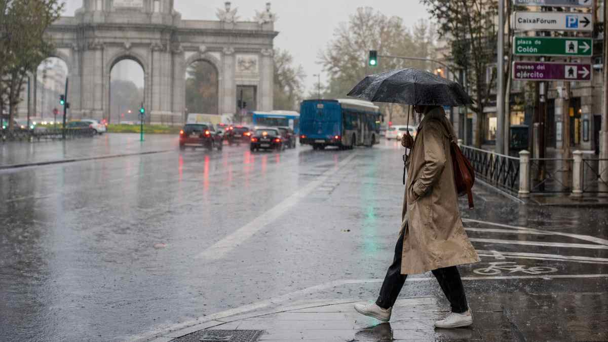 Lluvia intensa en Madrid con peatón cruzando bajo paraguas cerca de la Puerta de Alcalá