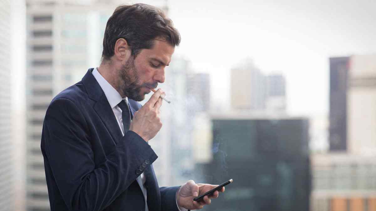 Trabajador fumando durante la jornada laboral mientras consulta el móvil en una pausa de trabajo
