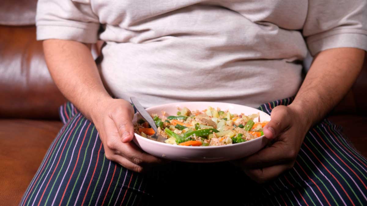 Persona con obesidad sostiene un plato de comida, relacionado con microbiota intestinal y obesidad
