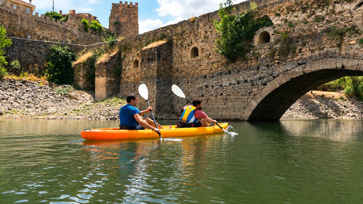 Personas practicando kayak en zona de baño oficial cerca de un puente histórico en Madrid