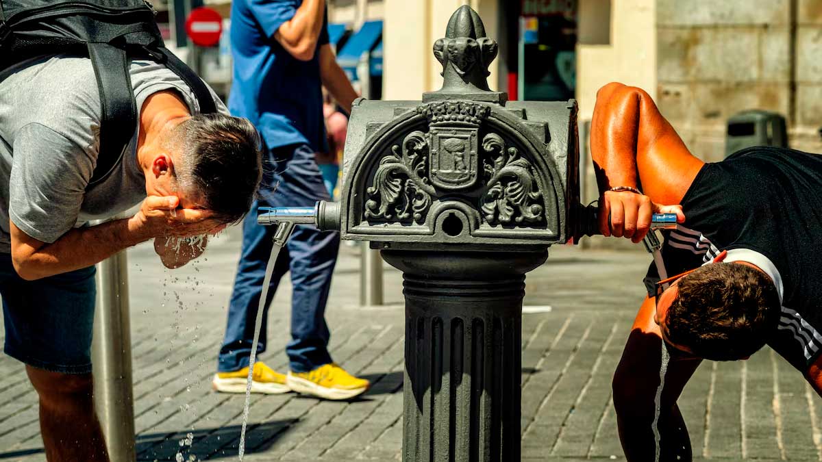 Personas refrescándose en una fuente pública durante aviso amarillo por calor en Madrid