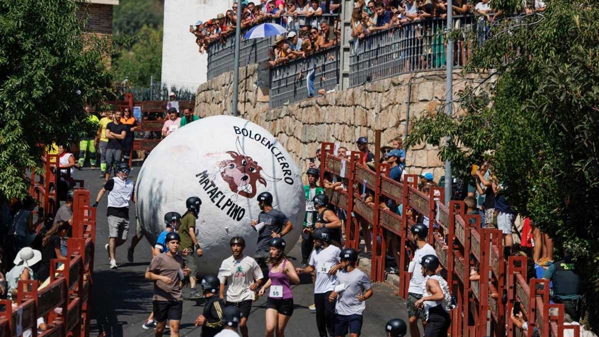 Corredores participan en el Boloencierro de Mataelpino delante de una gran bola blanca.