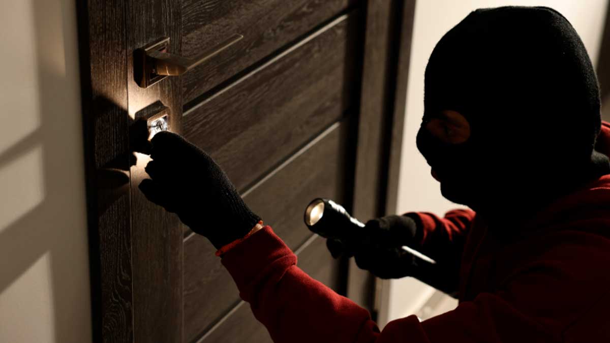 Ladrón forzando la cerradura de una vivienda durante un robo en sábado por la tarde